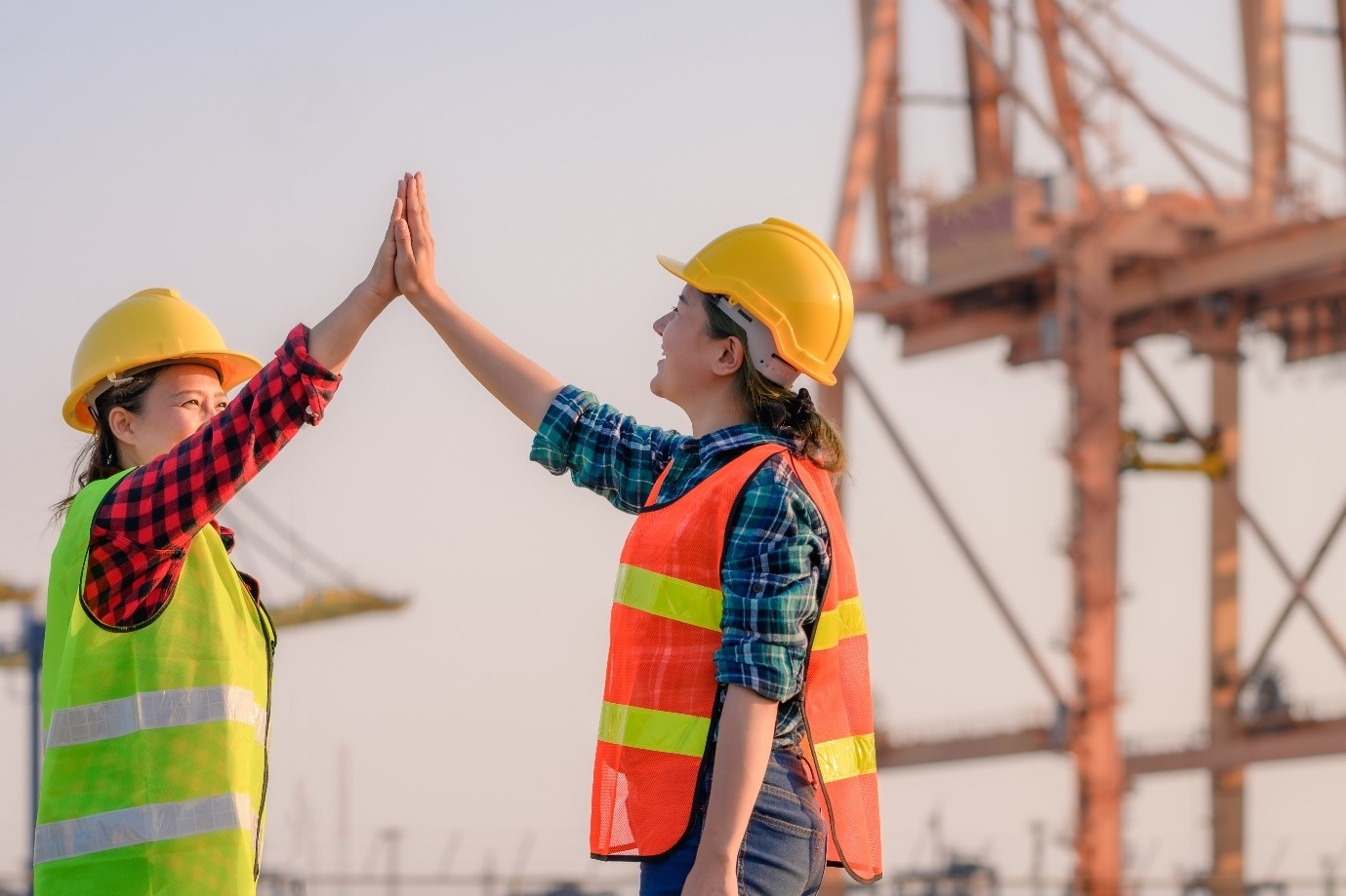 Two female port workers high fiving at a port with a crane in the background