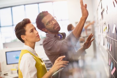 Two people in an office adding post-it notes onto the office wall